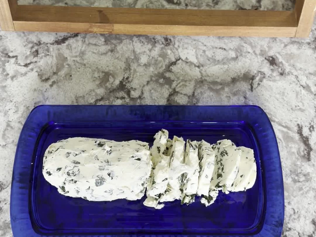 Chilled basil compound butter cut into small slices on a blue glass dish.