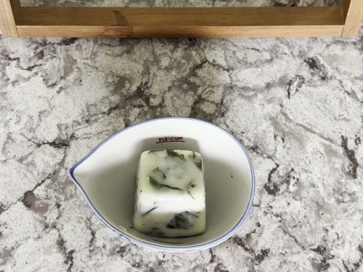 A frozen basil portion in a small bowl after removal from a cube tray.